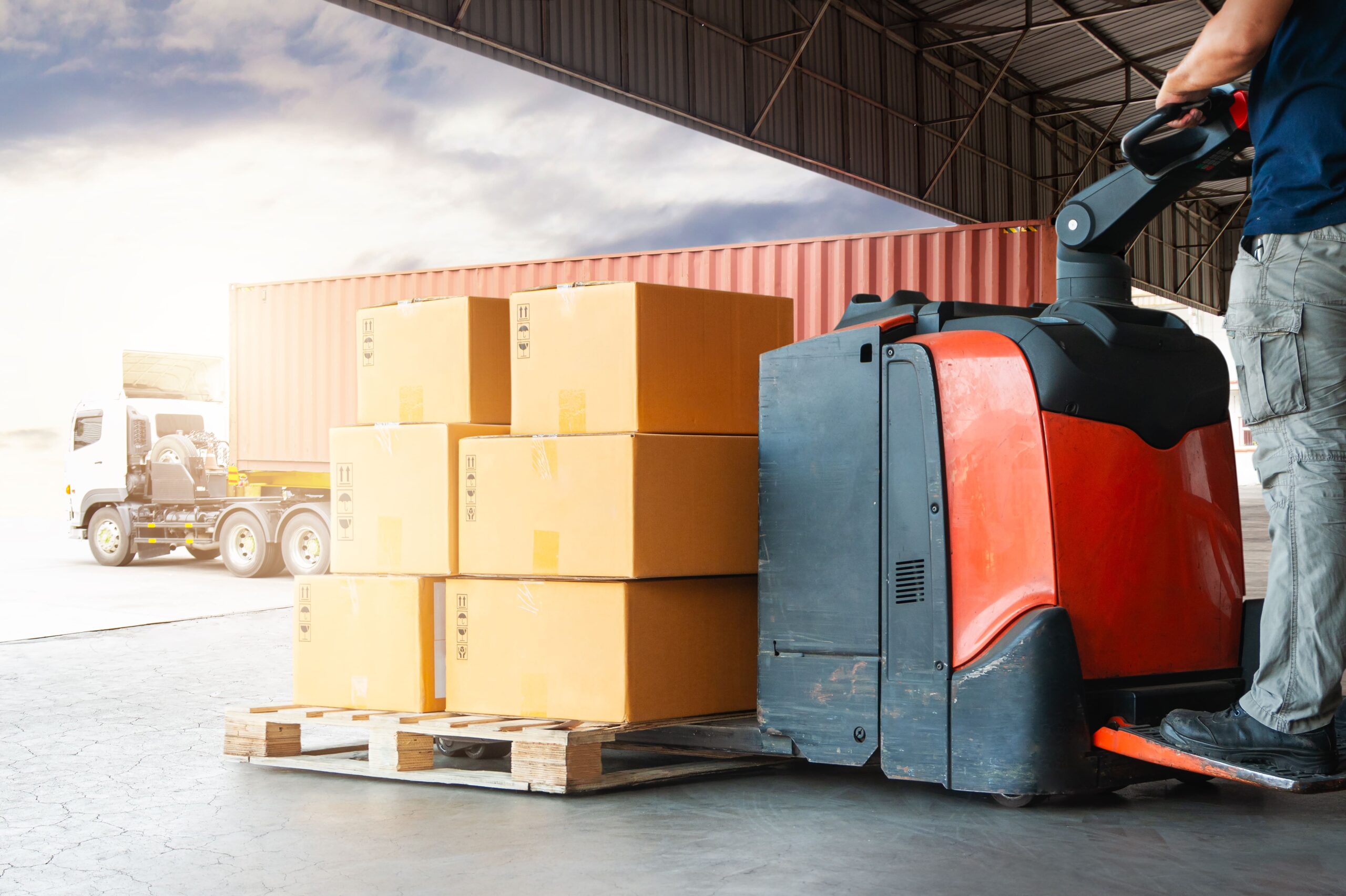 warehouse working using an electric pallet jack to haul boxes