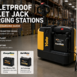 Electric pallet jack with an integrated on-board battery charger plugged into a standard 120V wall outlet inside a modern warehouse, demonstrating distributed charging without a dedicated battery room.